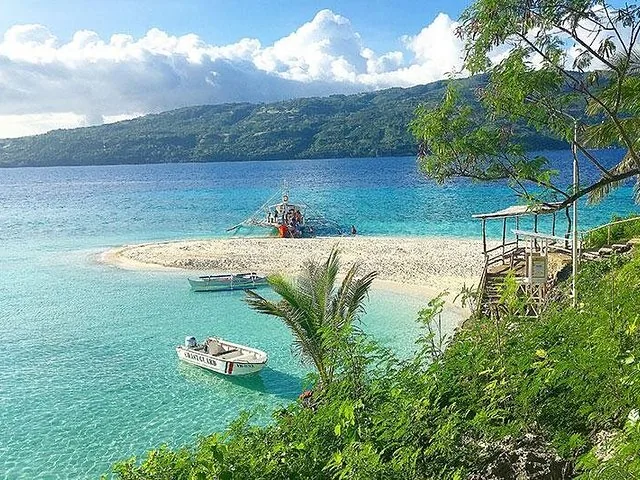 Boats moored near a white sandbar with lush green hills in the background.