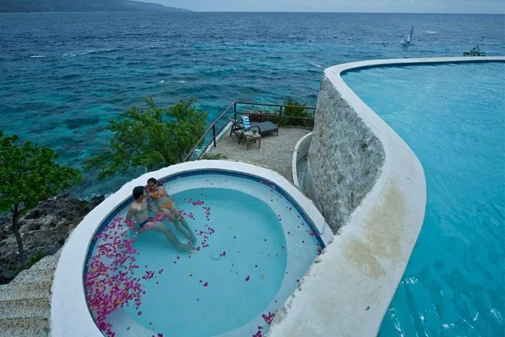 Couple relaxing in a circular infinity pool overlooking the ocean at a resort.