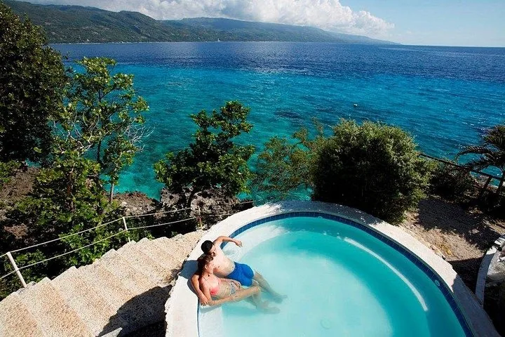 Couple lounging in a clifftop circular pool with stunning ocean views.