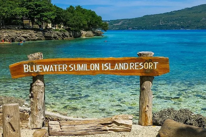 Wooden sign for Bluewater Sumilon Island Resort by the crystal-clear sea.