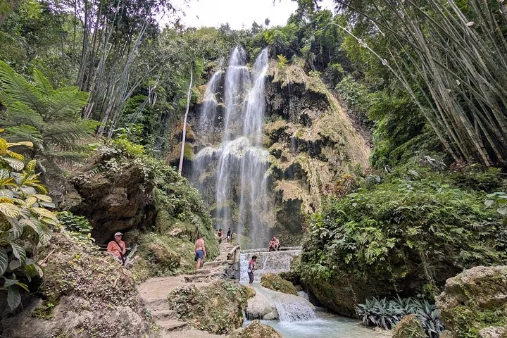 Visitors exploring the base of a multi-tiered waterfall surrounded by lush tropical forest.