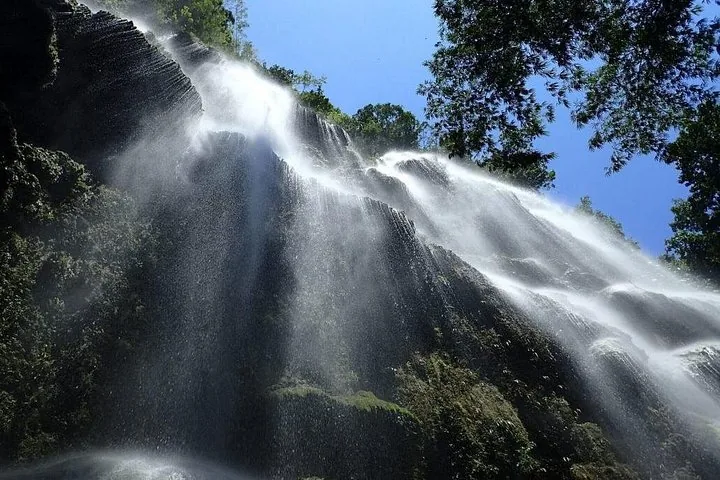 Powerful waterfall cascading down a rocky cliff surrounded by lush green foliage.